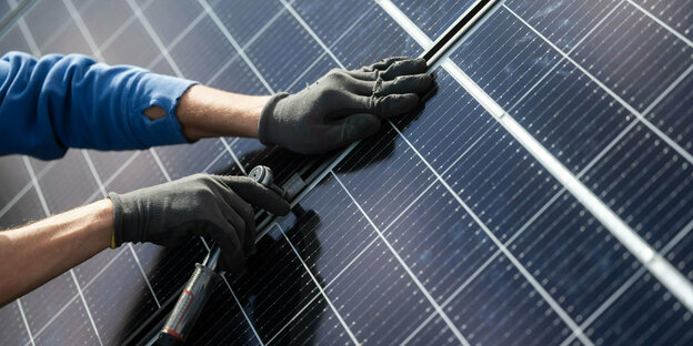 Egy férfi fotovoltaikus modulokat szerel össze egy lakóépület tetején.